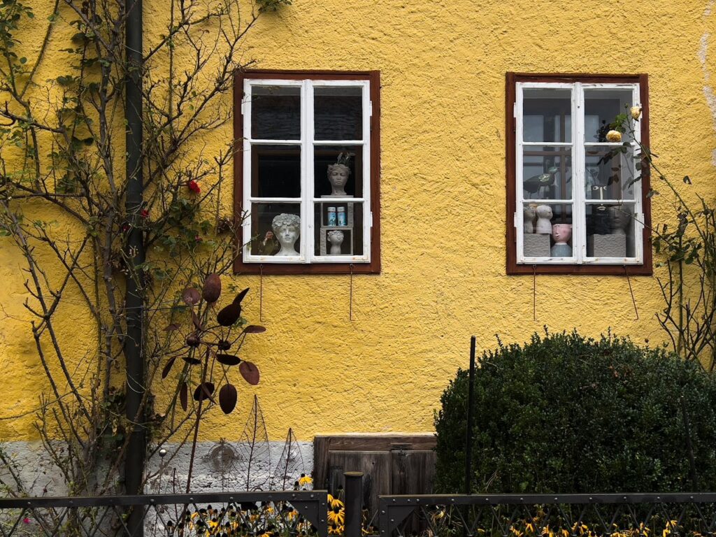 A vibrant yellow house facade with two white-framed windows displaying decorative busts.